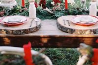 a winter wedding table setting with a greenery and fir runner, burgundy blooms and berries, red candles, wood slices
