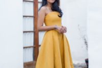 a yellow strapless midi dress with a high low skirt, pleats and navy velvet heels for a refined wedding guest look