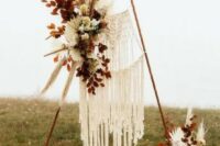 an amazing boho fall wedding arch with macrame, white and peachy blooms, dried leaves, pampas grass and dried fronds