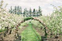 an apple orchard wedding ceremony space with a round floral arch and metal chairs that hint on the rustic theme of the wedding
