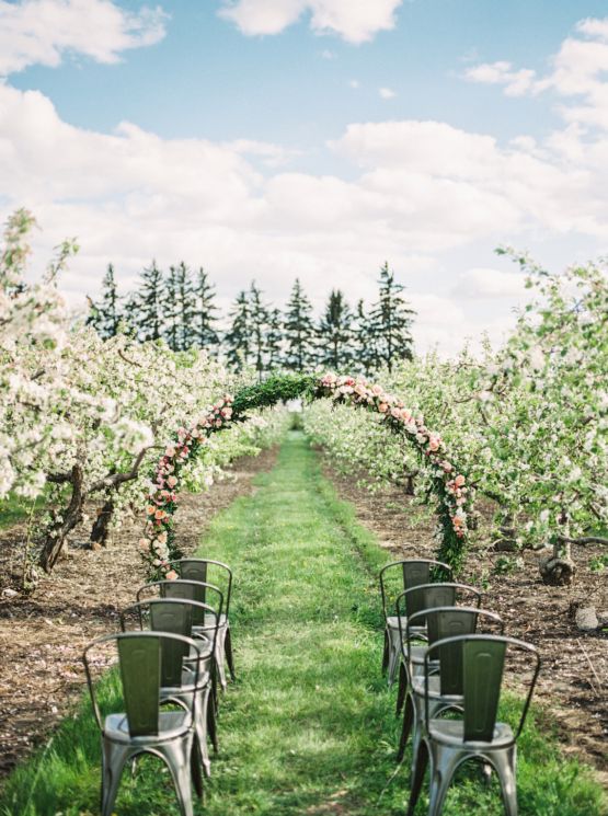 an apple orchard wedding ceremony space with a round floral arch and metal chairs that hint on the rustic theme of the wedding