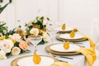 an elegant fall wedding tablescape with neutral and blush blooms and greenery, wooden chargers and white plates, marigold napkins and pears