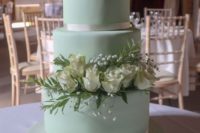 an elegant mint green wedding cake decorated with greenery, baby’s breath and white roses