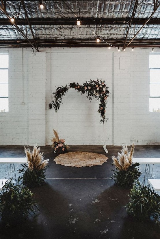 an industrial wedding ceremony space with hairpin leg benches, greenery and pampas grass is lovely idea