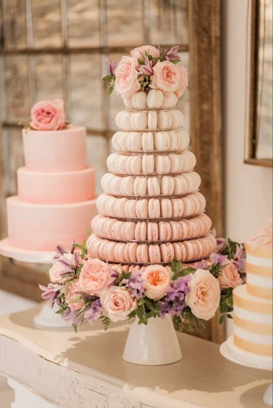 an ombre light pink macaron tower topped with blush blooms, purple ones and greenery is a very chic idea to go for