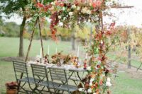 an outdoor wedding reception space with bold leaves, greenery, neutral and bright blooms over the table and next to it