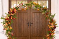ann oversized fall wedding wreath that can be used as a wedding arch, covered with greenery, bold leaves and bright orange, deep red and burgundy blooms