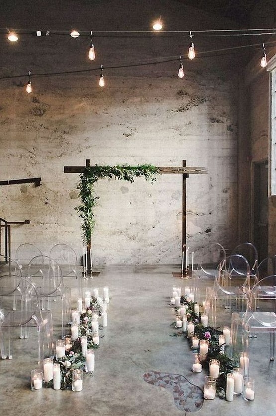candles and greenery to line up the aisle with ghost chairs and a wedding arch decorated with greenery