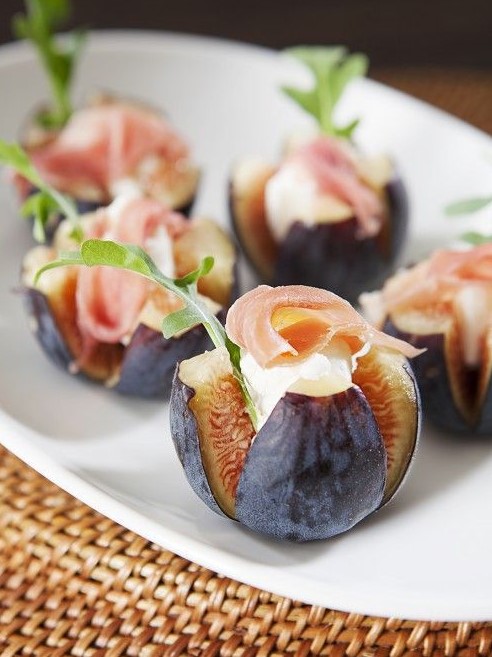 cut figs topped with cheese, proschiutto and arugula are a non-traditional appetizer for the fall