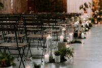 metal and wood folding chairs and aisle decor with greenery and candles for a modern industrial wedding space