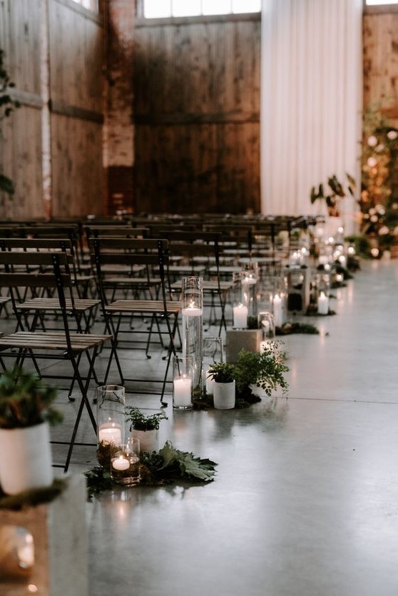 metal and wood folding chairs and aisle decor with greenery and candles for a modern industrial wedding space