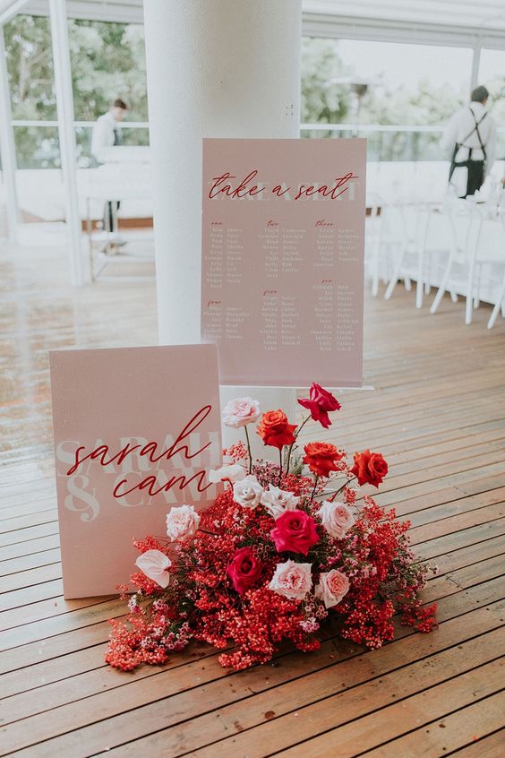 pink and red wedding decor with pink signs with red calligraphy and a lush red and blush floral arrangement is wow