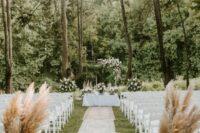 white folding chairs, greenery and pampas grass and boho grugs along the wedding aisle are a great combo for a boho wedding