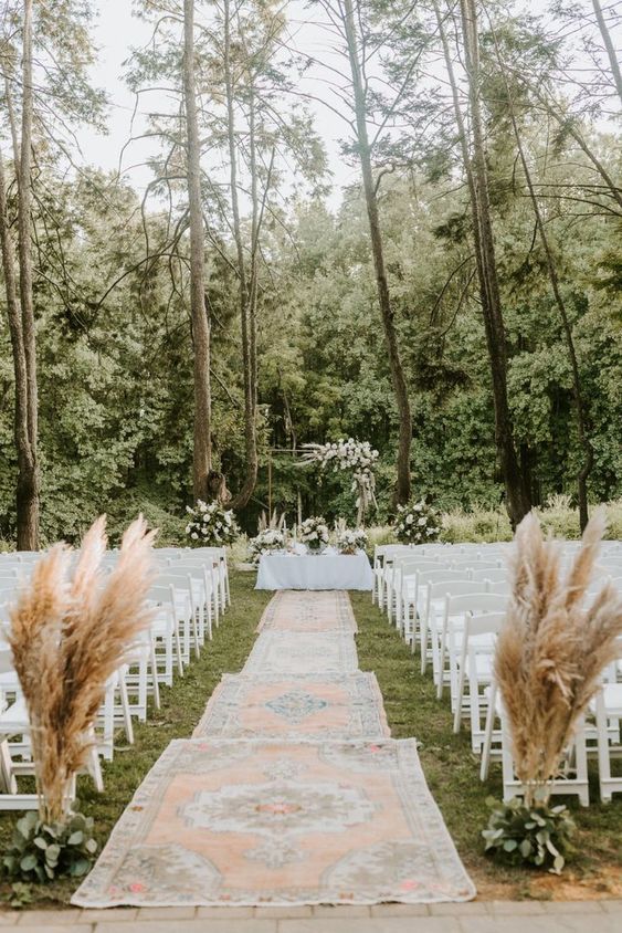 white folding chairs, greenery and pampas grass and boho grugs along the wedding aisle are a great combo for a boho wedding