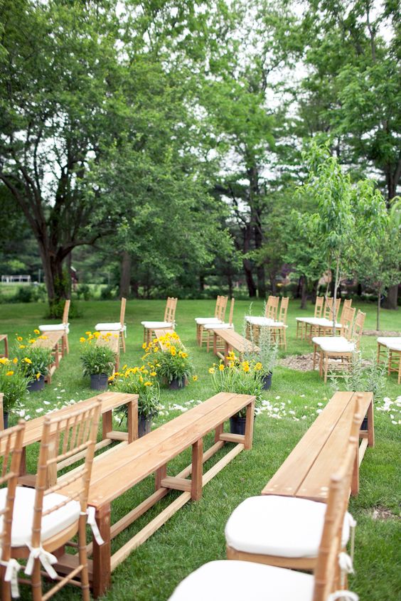 wooden benches and chairs with white upholstery, potted blooms and petals on the aisle are a great combo for a garden wedding