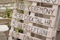 a DIY timeline wedding sign made of a whitewashed pallet with burlap bows and some greenery hanging down