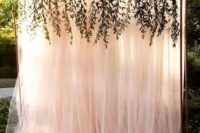 a beautiful blush tulle wedding backdrop with some greenery hanging down from copper piping