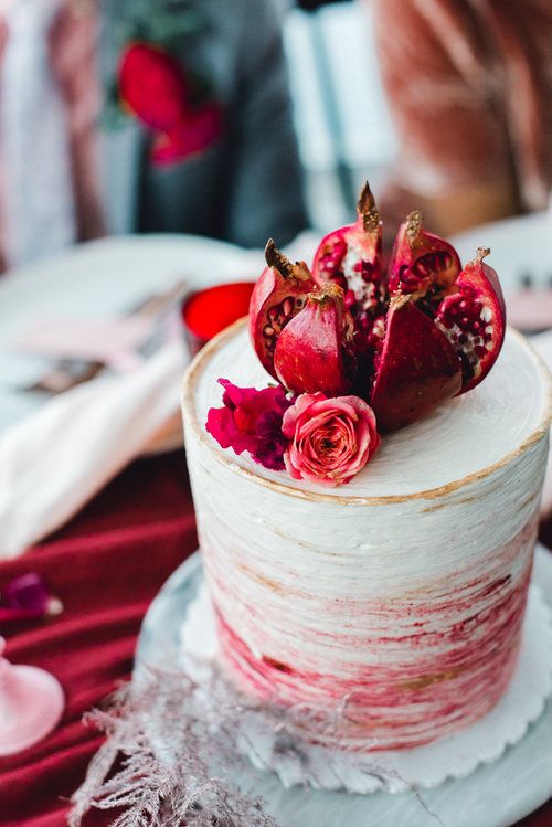 a beautiful hand painted ombre wedding cake with a gold edge, deep red blooms and a cut pomegranate on top is ideal for a fall wedding