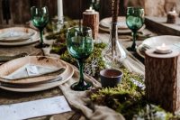 a boho wedding tablescape with a greenery and moss runner, candles, tree branches, feathers and tall and thin candles