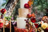 a bold fall wedding cake with pomegranates, burgundy blooms, bold fall leaves and berries, with white, gold and burgundy petal tiers