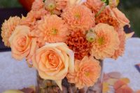 a bold fall wedding centerpiece of a glass filled with acorns, bold orange and rust blooms is a cool idea to go for