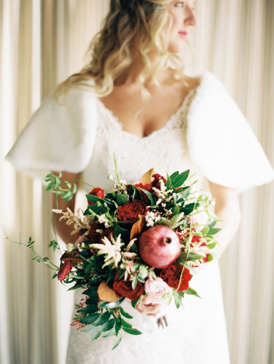 a bold wedding bouquet of greenery, pink and deep red blooms, a pomegranate to give the arrangement a bold look