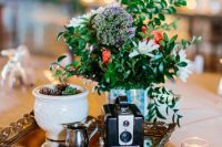 a bold wedding centerpiece of a tray with bold blooms and greenery, a bowl with succulents, a vintage camera is a lovely idea to DIY