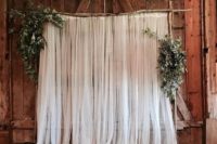 a branch, tulle curtains and greenery wedding backdrop is a cozy rustic piece for wedding decor