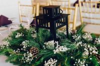 a candle lantern surrounded with evergreens, pinecones and baby’s breath is a lovely and fresh wedding centerpiece