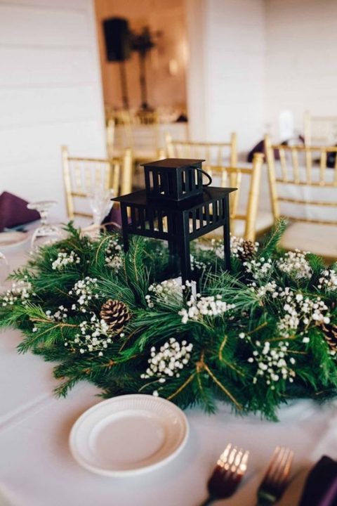 a candle lantern surrounded with evergreens, pinecones and baby's breath is a lovely and fresh wedding centerpiece