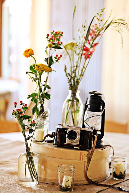 a catchy wedding centerpiece of a round wooden box with candles, bright blooms and greenery, a lantern and a vintage camera