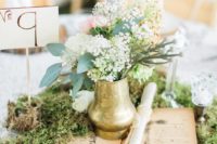 a chic vintage-inspired wedding centerpiece with moss, an open book, a gilded vase and blooms plus a table number