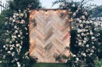 a chic wedding backdrop built of pallet wood clad with a herringbone pattern, lights and lush florals and greenery around