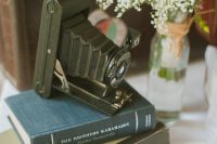 a chic wedding centerpiece of a book stack, a vintage camera and a baby’s breath arrangement is a lovely idea for a vintage wedding