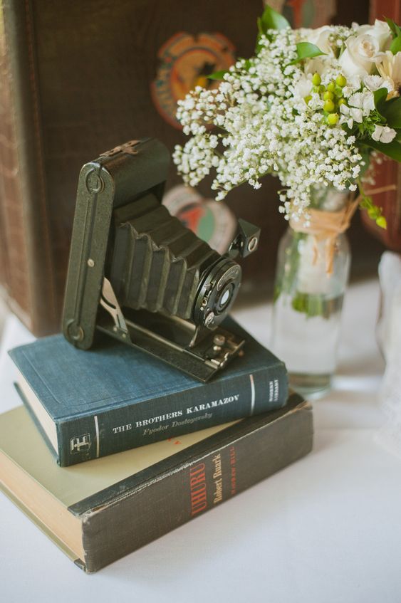 a chic wedding centerpiece of a book stack, a vintage camera and a baby's breath arrangement is a lovely idea for a vintage wedding