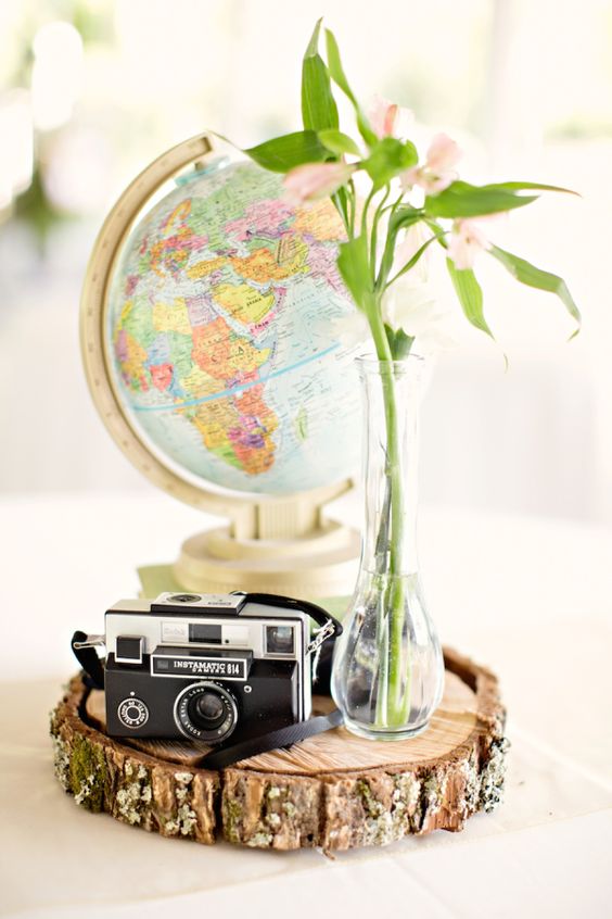 a creative wedding centerpiece of a wood slice, a vintage camera, a blush bloom arrangement and a globe is a lovely idea for a travel-themed wedding