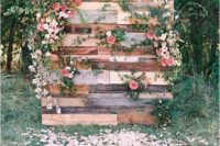 a cute pallet wedding backdrop with lush blooms and greenery plus petals all around looks very romantic