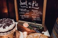 a cute rustic pie bar with greenery, blush roses, candles, a chalkboard sign in a frame and some pies on stands