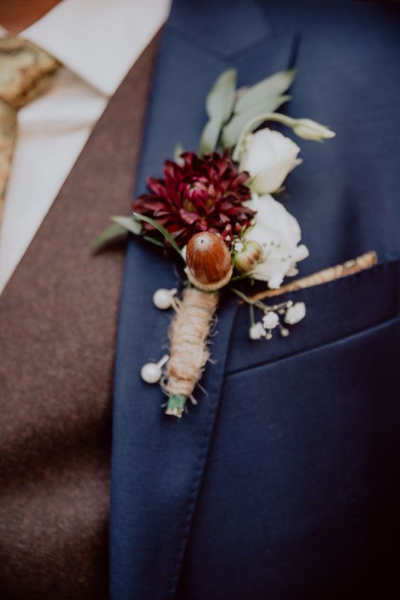 a fall wedding boutonniere with white and burgundy blooms, greenery and acorns, pins and twine is a cool accessory to go for