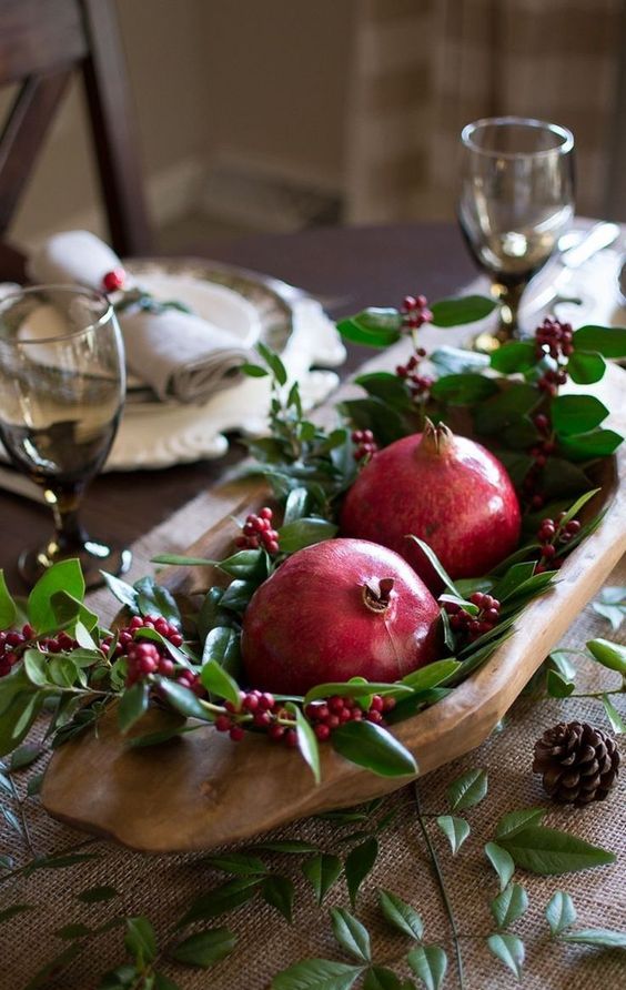 a fall wedding centerpiece of a wooden bowl, greenery, berries and pomegranates is a lovely idea for a fall rustic wedding
