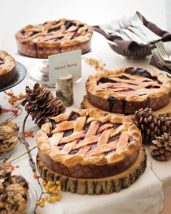a fall wedding pie bar done with wooden slices as pie stands, bold blooms and berries and pinecones is a very cool and chic idea