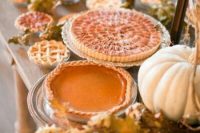 a fall wedding pie bar with dried leaves, pumpkins and some delicious fall-inspired pies
