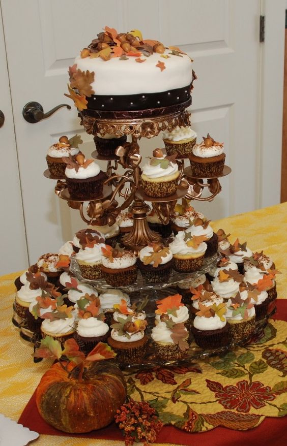 a fall wedding sweets stand of tiered plates, cupcakes and a wedding cake topped with bold fall leaves and acorns is a great idea