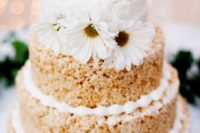 a krispie rice wedding cake with cream, a buttercream tier and white blooms on top for a rustic wedding