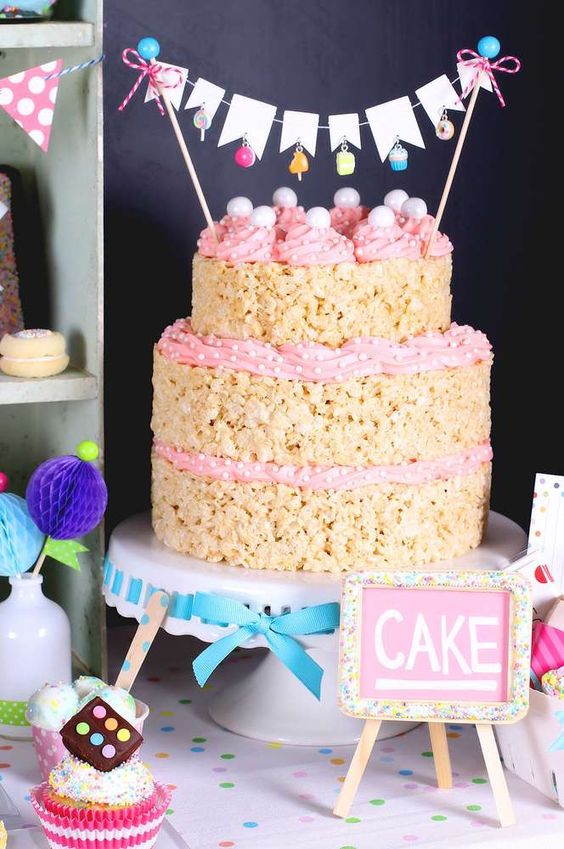 a krispie rice wedding cake with pink cream, confetti and mini pink cones on top