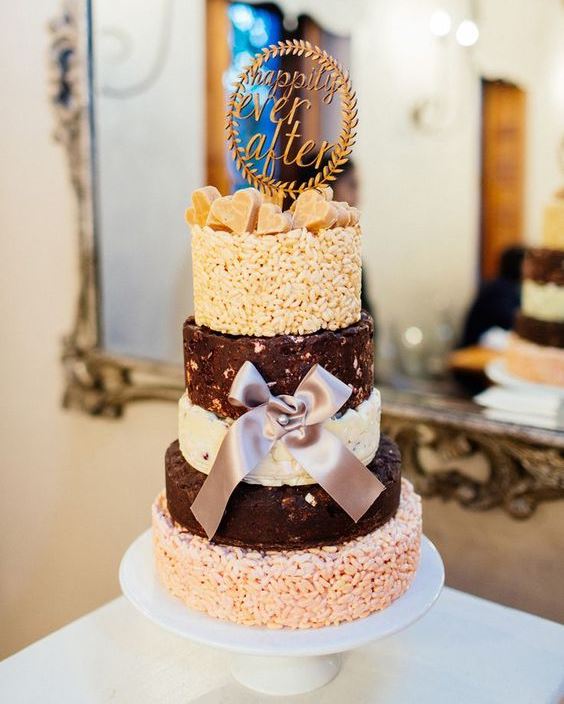 a krispie rice wedding cake with white and dark chocolate tiers, edible hearts on top, a creative topper and a silk bow