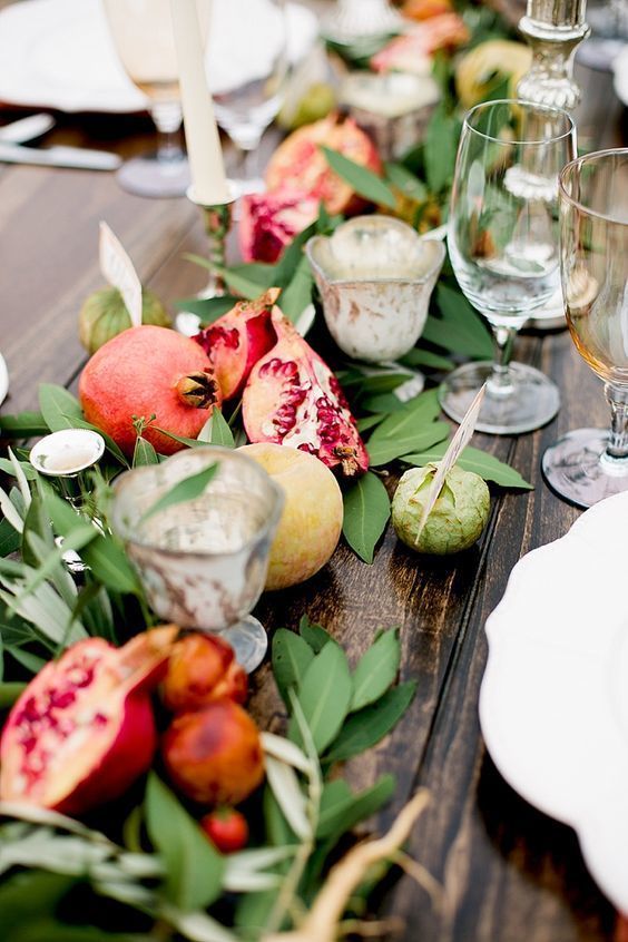 a lovely fall wedding table runner with greenery, apples, pomegranates, candles of various kinds in vintage candleholders