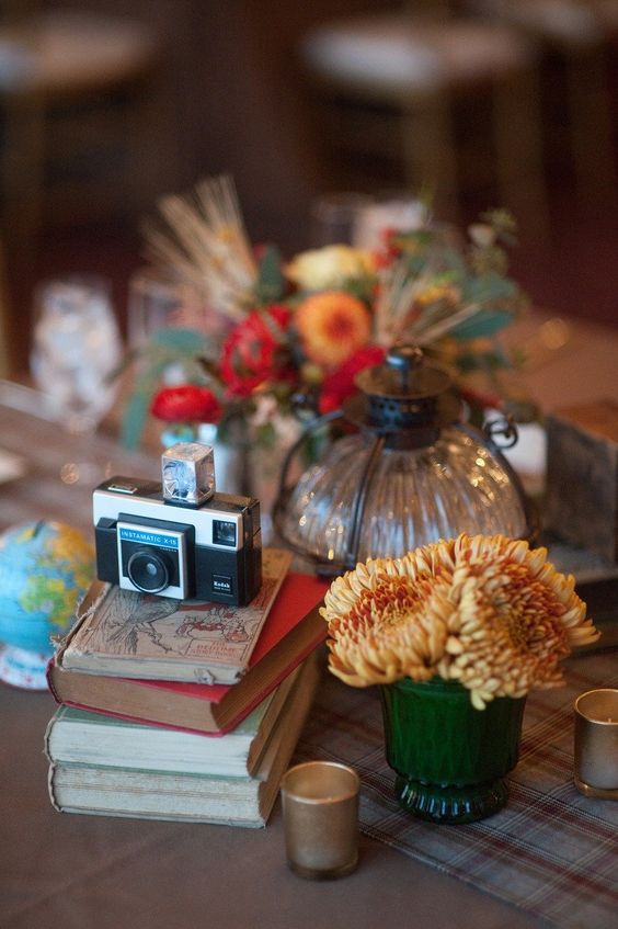 a lovely wedding centerpiece of a stack of vintage books, a vintage camera, bold blooms and a small globe is all chic