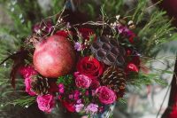 a moody fall wedding bouquet with pink and red blooms, greenery, pomegranates and pinecones plus lotus slices