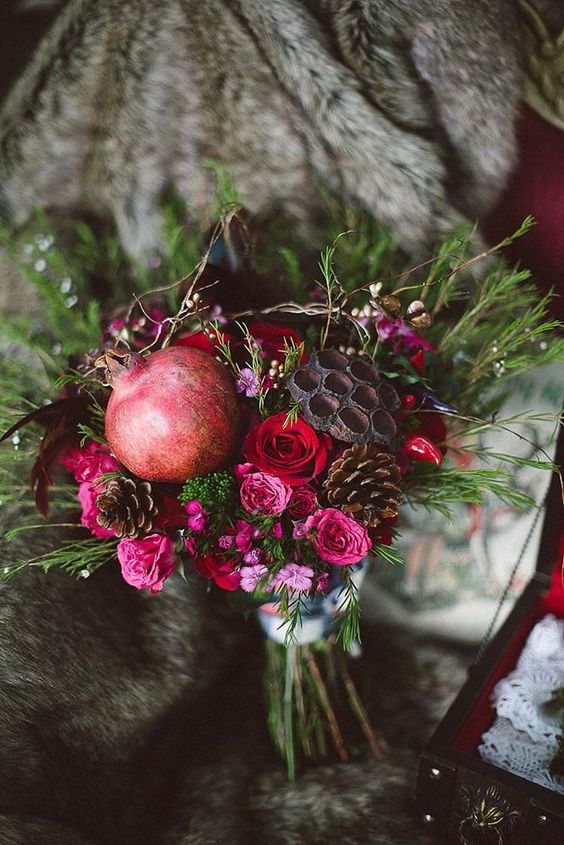 a moody fall wedding bouquet with pink and red blooms, greenery, pomegranates and pinecones plus lotus slices